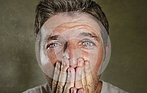 Head and shoulders dramatic portrait of young man crying in pain suffering depression and anxiety problem covering his mouth with