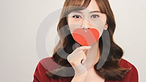 Head and shoulders portrait of attractive Asian woman looking at camera with deep gray eyes while covering her mouth with heart