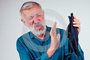 Head and shoulders portrait of a senior man scrunching up his face while holding his nose and holding smelly socks in