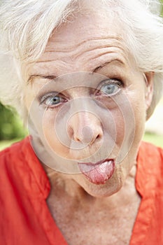 Head And Shoulders Portrait Of Senior Woman Poking Out Tongue