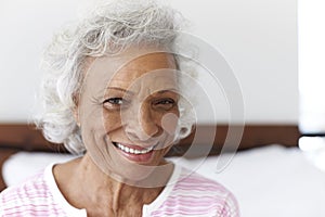 Head And Shoulders Portrait Of Smiling Senior Woman Sitting On Bed At Home Looking Positive