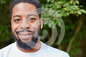 Head And Shoulders Portrait Of Smiling Young Man Standing Outdoors In Garden