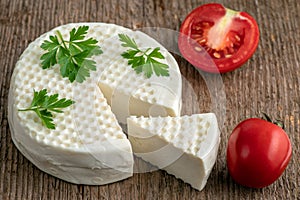 Head and slice of brined cheese, bryndza, on a wooden background with tomatoes and parsley.