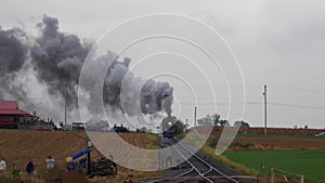 Head on view of a steam locomotive pulling freight pulling into yard with smoke and steam