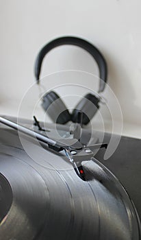 Head Of Vinyl Record Player On Disc In Front Of Defocused Black Headphones On White Background