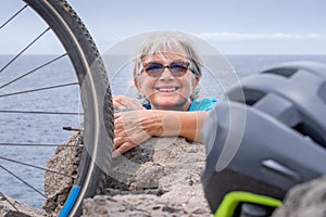 The head of a woman cyclist pokes out of the rocks after a hike with her electric bike. Mature woman smiles happily