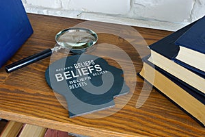 Head with words beliefs on the shelf and magnifying glass.