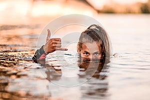 Head of young woman half emerges from the water and her hand shows gesture