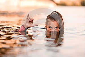 Head of young woman half emerges from the water and her hand shows gesture of greeting