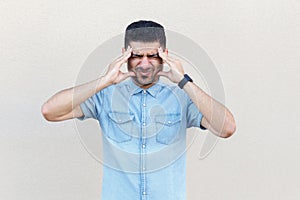 Headache, confusion or problem. Portrait of sick handsome young bearded man in blue shirt standing and holding his head and