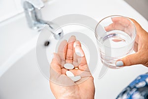 Headache hand with pills medicine tablets and glass of water against white background