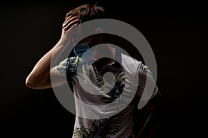 Headache man in blue medical mask isolated black background. Man touches her head because sicks coronavirus covid-19 photo