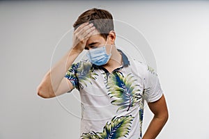 Headache man in blue medical mask isolated white background. Man touches her head because sicks coronavirus covid-19