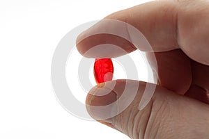 Headache pain relief, pharmaceutical treatment and sickness fighting concept with close up fingers holding red gel capsule