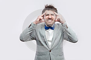 Headache. Portrait of sick or worry bearded man in casual grey suit and blue bow tie standing and holding his painful head with