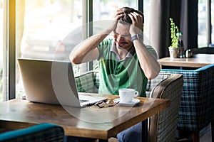 Headache, problem or confusion! Young businessman in green t-shirt sitting and holding his painful head. business and freelancing