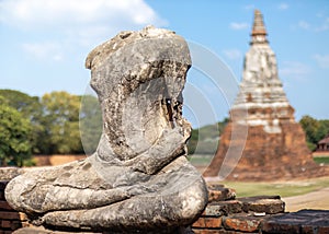 Headless and armless statue of Buddha seated in lotus position made of stone, stupa made of brick behind. Thai Buddhist temple in