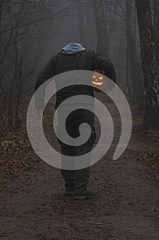 Headless man with Halloween pumpkin in foggy forest