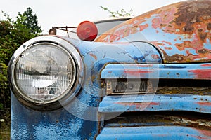 Headlight and grille on a rusty blue antique truck