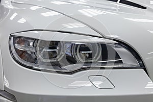 Headlight with lining view of luxury very expensive new white BMW X6 M Lumma CLR tuning car stands in the washing box waiting for