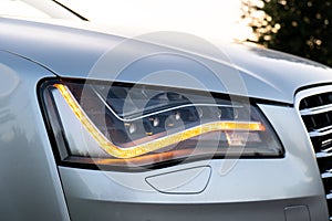 Headlight turned on in Clean car after Washing luxury silver car. Sedan car exterior of modern luxury car during sunset