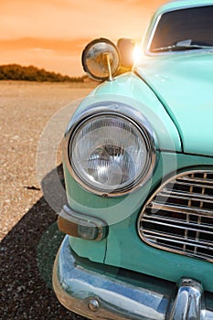 Headlight of a vintage classic car in the autumn golden sky at sunset time.