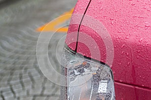 Headlights of a red car with raindrops