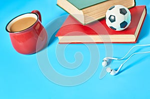 .Headphone, old books, toy basketball ball and red cup full of coffee on blue background