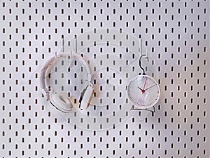 Headphones and Alarm Clock Hanging on White Perforated Wall