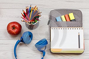 Headphones, apple, metal stand with color pencils and open exercise book on bag-pencil case with color felt pens and marker