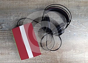 Headphones and book. The book has a cover in the form of Latvia flag.