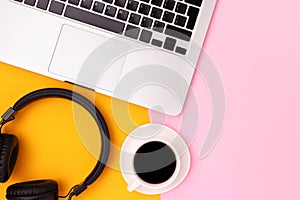 Headphones, cup of black coffee and laptop on a yellow and pink background..