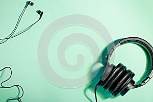 Headphones of different types flat lay on mint color background, copy space. Black in ear headphones and foldable over