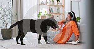 Headphones, dog playing and woman in a living room feeling puppy love from pet care in a home. House, animal and young