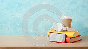 Headphones, smartphone, stack of books and paper cup on a table