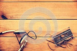 Headphones and translucent audio cassette tape on vintage wood planks background