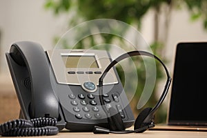 Headset, desktop telephone and laptop on table indoors. Hotline concept