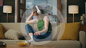 Headset lady listening music smiling sofa. Happy girl enjoying song dancing beat