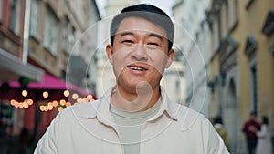 Headshot adult asian man in protective medical mask stands in the city outdoors taking off respirator take deep breath