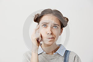 Headshot of adult girl looking up with frown expressing misunderstanding. Cute female student twisting mouth trying to