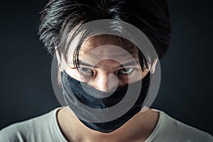 Headshot of Asia man wearing a cloth face mask as protection against transmission, infection. Dark background