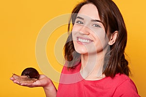 Headshot of attractive female holds Achatina snail on her palm, demonstrates trughtful feelins, dressed in casual clothes, looks