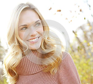 Headshot of a beautiful blonde woman standing in a park in fall. Happy attractive young female smiling outside on an