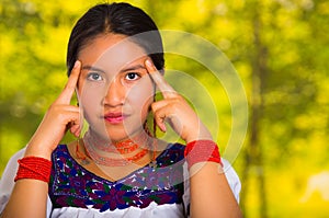 Headshot beautiful young woman wearing traditional andean blouse with red necklace, posing for camera touching face