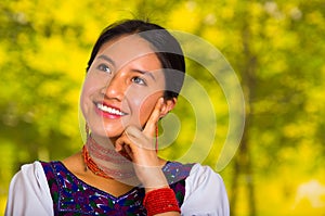 Headshot beautiful young woman wearing traditional andean blouse with red necklace, posing for camera touching face