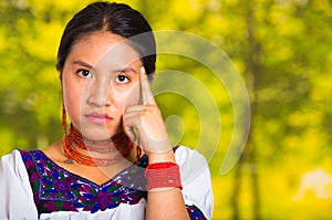 Headshot beautiful young woman wearing traditional andean blouse with red necklace, posing for camera touching face