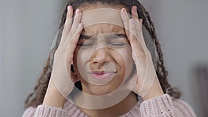 Headshot of burnt out fatigued African American teen girl rubbing temples having headache migraine. Close-up of
