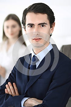 Headshot of businessman standing straight with colleagues at background in office. Group of business people discussing