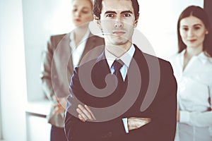 Headshot of businessman standing straight with colleagues at background in office. Group of business people discussing