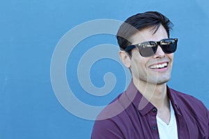 Headshot of a Caucasian man in his mid twenties with designer sunglasses taken against a plain blue background with copy space